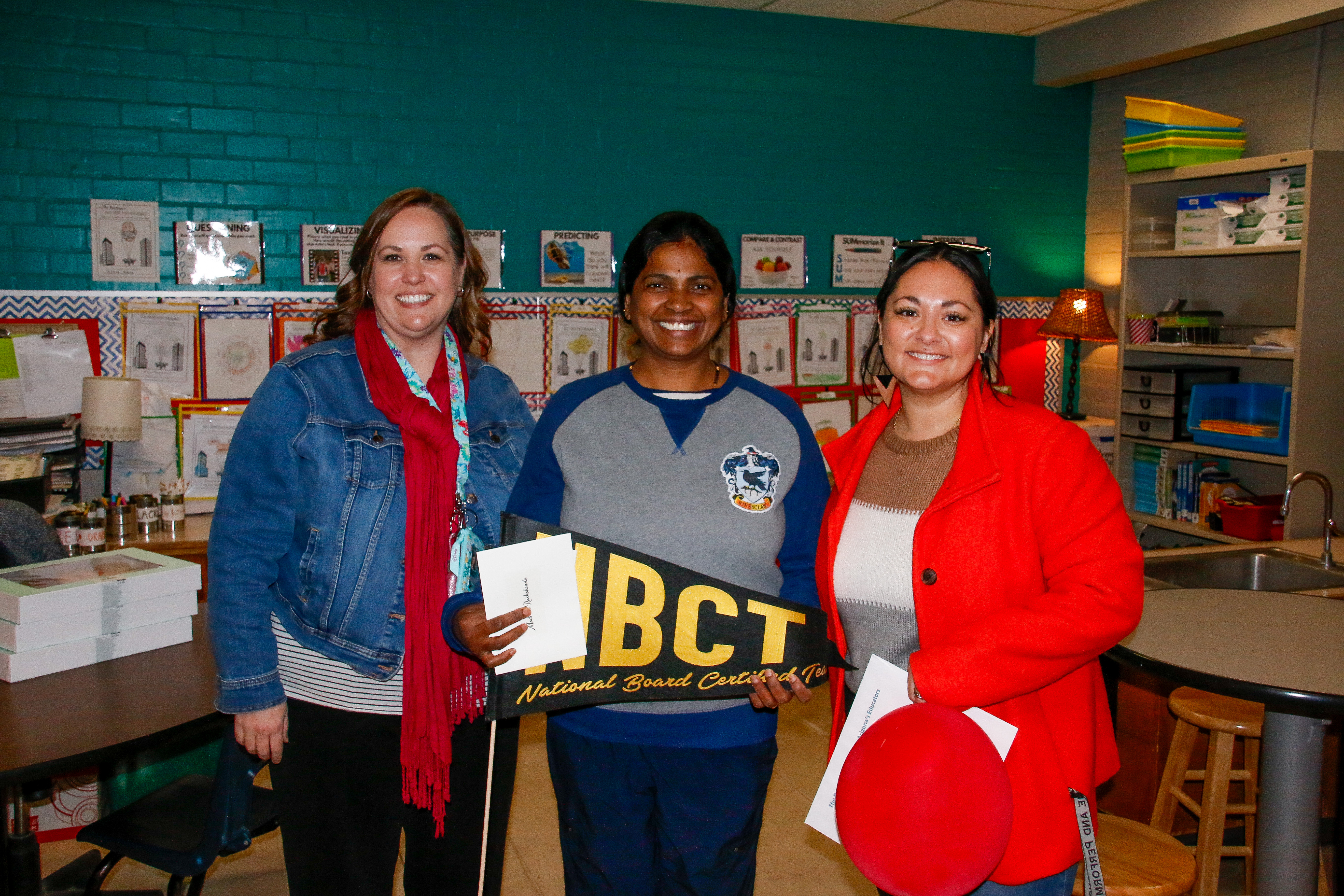 A woman, center, holds an NBCT pennant, while a woman on each side of her smiles