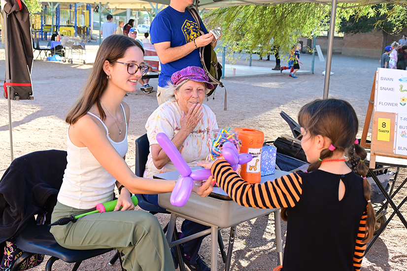 A woman in glasses hands a young girl a purple balloon animal