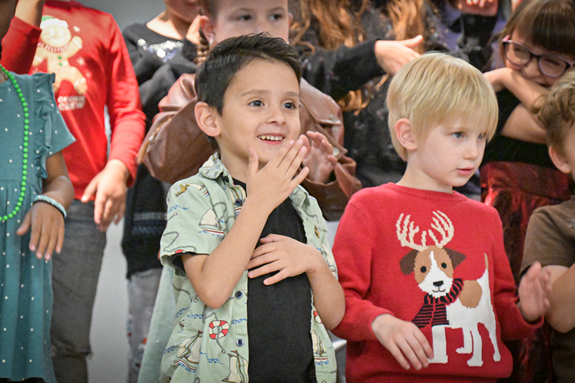 A boy holds his hand in front of his mouth as he and his classmates perform a song