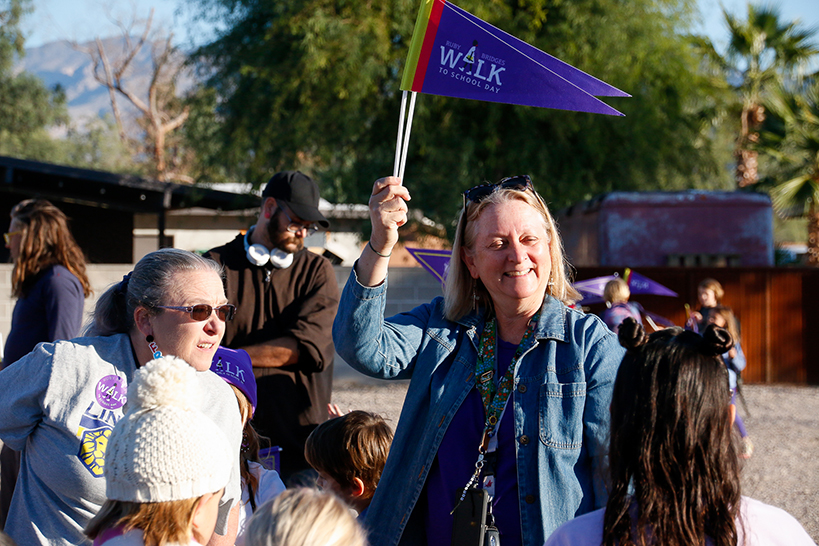 A woman smiles as she holds up two purple Ruby Bridges Walk to School pennants
