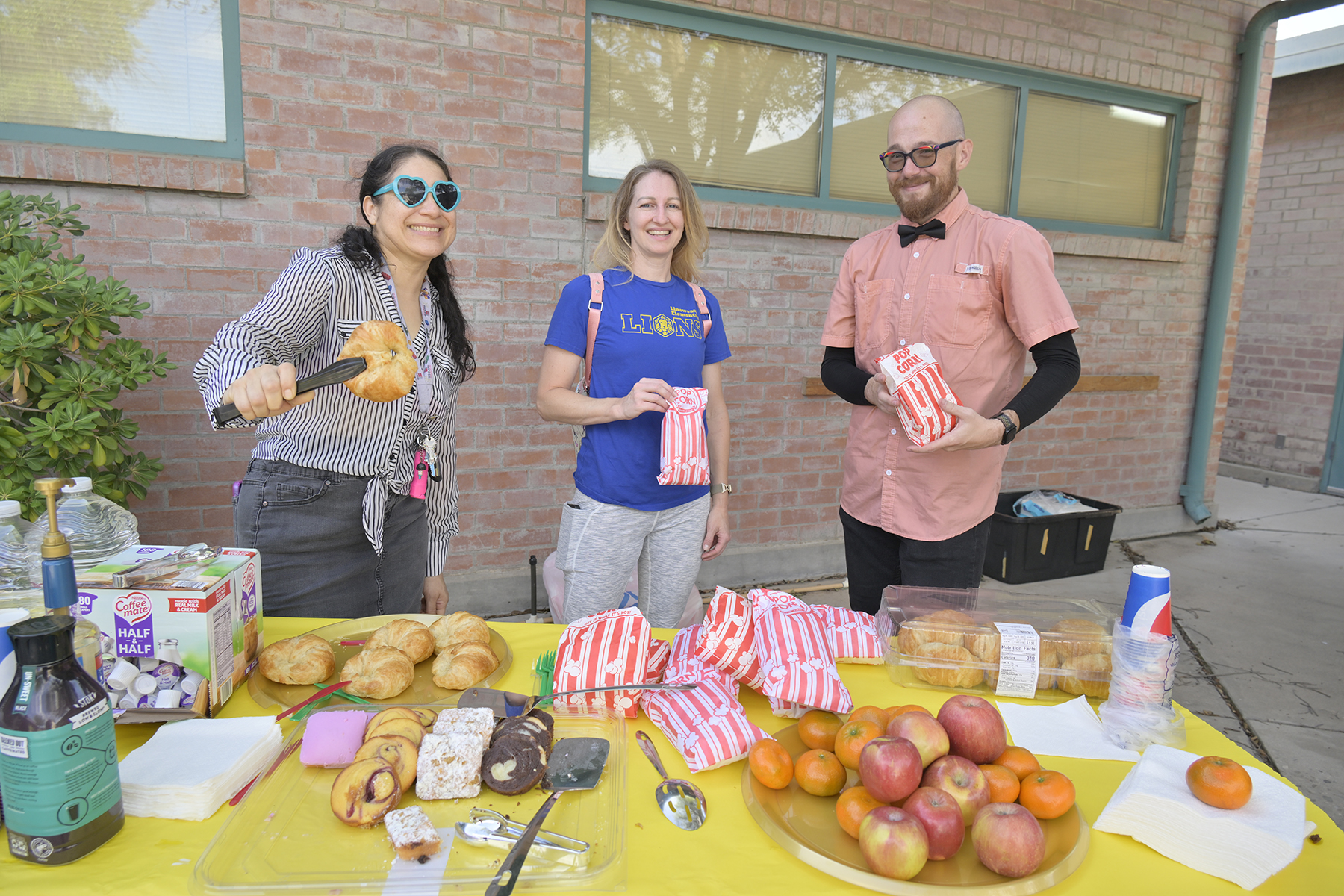 Three staff members hold up snacks for students